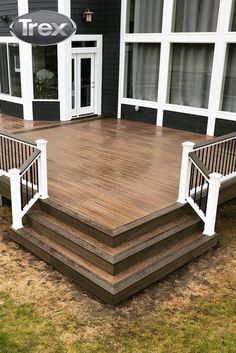 a wooden deck with white railings in front of a black house and grass area