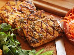 some food is laying out on a cutting board with carrots and other foods in the background