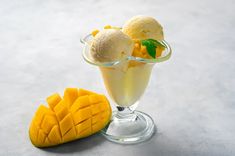 two scoops of ice cream with mango slices in a glass on a gray surface