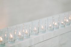 candles are lined up in rows on a ledge next to a wall with white marble