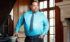 a man in a blue shirt and tie standing next to a piano