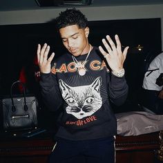 a young man is holding his hands up in the air while wearing a black sweatshirt with an image of a cat on it