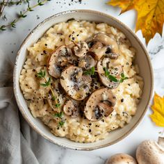 a bowl filled with rice and mushrooms on top of a white table next to autumn leaves