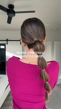 a woman with long hair in a ponytail wearing a pink sweater and standing in front of a ceiling fan