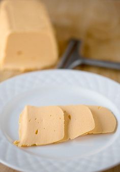 three slices of cheese on a white plate with a knife and fork in the background