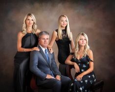 three women and one man are posing for a family portrait in front of a dark background