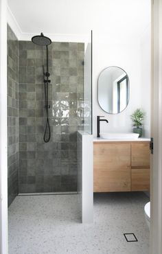 a bathroom with a walk in shower next to a white sink and wooden cabinet under a round mirror