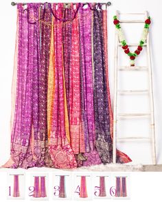 an assortment of different colored fabrics hanging on a wall next to a ladder and flower garland