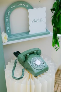 an old fashioned green phone sitting on top of a table next to a potted plant