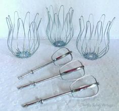 four metal utensils sitting on top of a white tablecloth covered table next to each other