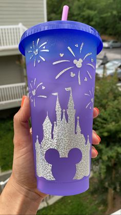 a person holding up a purple cup with mickey mouse's castle painted on it