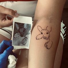 a person with a tattoo on their arm holding up an inked photo next to a drawing of a dog