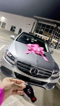 a person holding a car key in front of a mercedes dealership with a pink bow on it