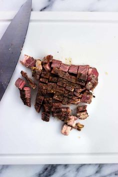 sliced up meat sitting on top of a white cutting board with a knife next to it