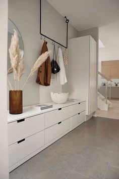 a room with white cabinets and coat racks on the wall next to a vase filled with dry grass