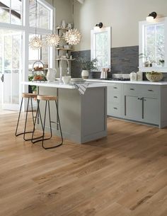 a large kitchen with wooden floors and white walls, two stools in front of the island