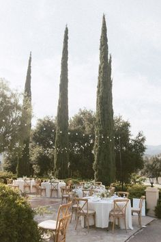 an outdoor dining area with tall trees and white tablecloths set for two people