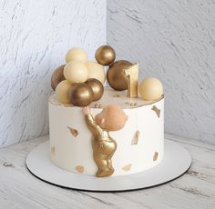 a white cake with gold decorations and a little boy reaching up to it on top