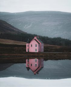 a pink house sitting on top of a lake next to a lush green mountain covered in trees