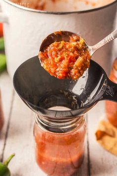 a spoon full of chili sauce on top of a pot filled with peppers and other ingredients