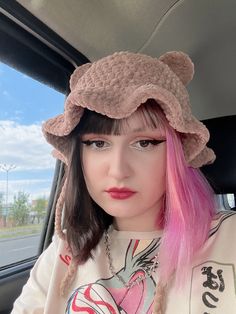 a woman with pink hair wearing a bear hat in the back seat of a car