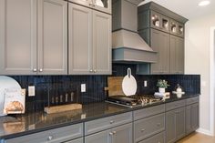 a kitchen with gray cabinets and black counter tops, including a white cutting board on the stove