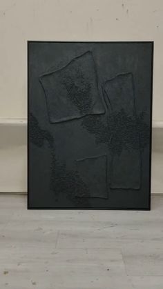 a black painting sitting on top of a hard wood floor next to a white wall