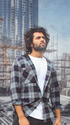 a man with long hair wearing a jacket and jeans standing in front of a cityscape