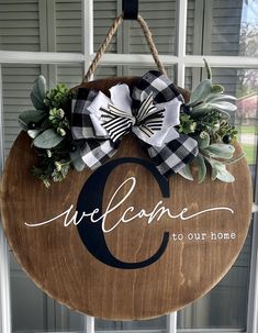 a wooden sign hanging on the front door with a bow and welcome to our home