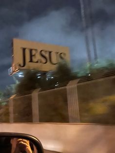 the reflection of a person in a car's side view mirror as they drive past a jesus sign