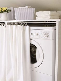 a washer and dryer sitting in front of a white cabinet with curtains on it