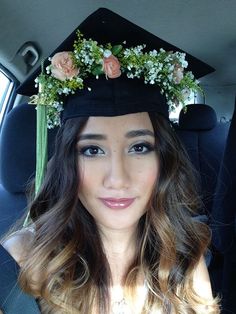 a young woman wearing a graduation cap with flowers on it's head is sitting in the back seat of a car