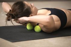 a woman laying on top of a yoga mat with two green balls in her hand