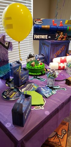 a purple table topped with lots of toys and cake next to a yellow ballon