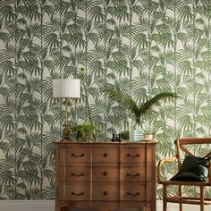 a living room with palm leaves on the wall and a wooden dresser in front of it