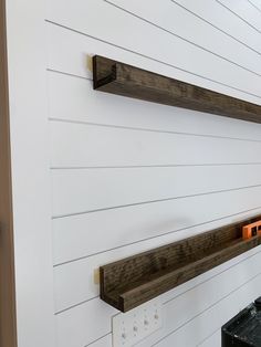 two wooden shelves on the side of a white wall next to a black box with an orange light in it