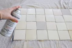 someone using a spray can to paint white tiles on a bed sheet that has been made into a mosaic pattern