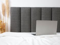 an open laptop computer sitting on top of a bed next to a tall headboard