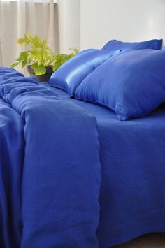 a bed with blue sheets and pillows next to a potted plant