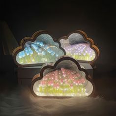 three lit up clouds sitting on top of a white box filled with pink and blue flowers