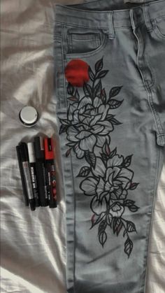 a pair of jeans with flowers painted on them next to some pens and marker markers