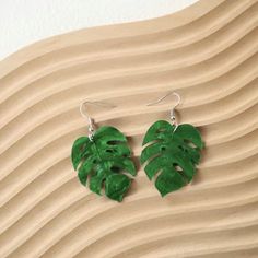 a pair of green leaf shaped earrings on top of a wooden surface with wavy waves