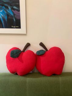 two red apples sitting on top of a green couch in front of a framed painting