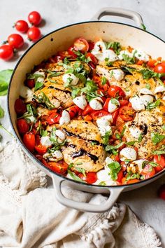 a pan filled with chicken and tomatoes on top of a white cloth next to cherry tomatoes