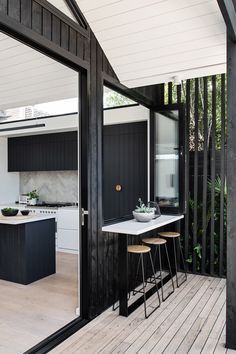 an outdoor kitchen and dining area with wooden flooring, black painted cabinets and white walls