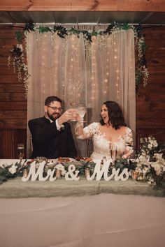 a bride and groom toasting at their wedding reception with mr & mrs sign in the background