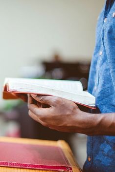 a man holding a book in his hands while standing next to a table with an open book on it