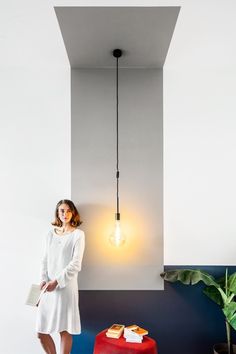 a woman standing next to a red stool in a room with a light bulb hanging from the ceiling