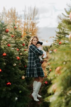 a woman holding a cat in her arms while walking through a christmas tree lot at the farm