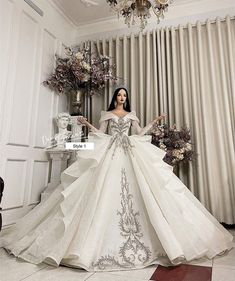 a woman in a white dress standing next to a chandelier with flowers on it